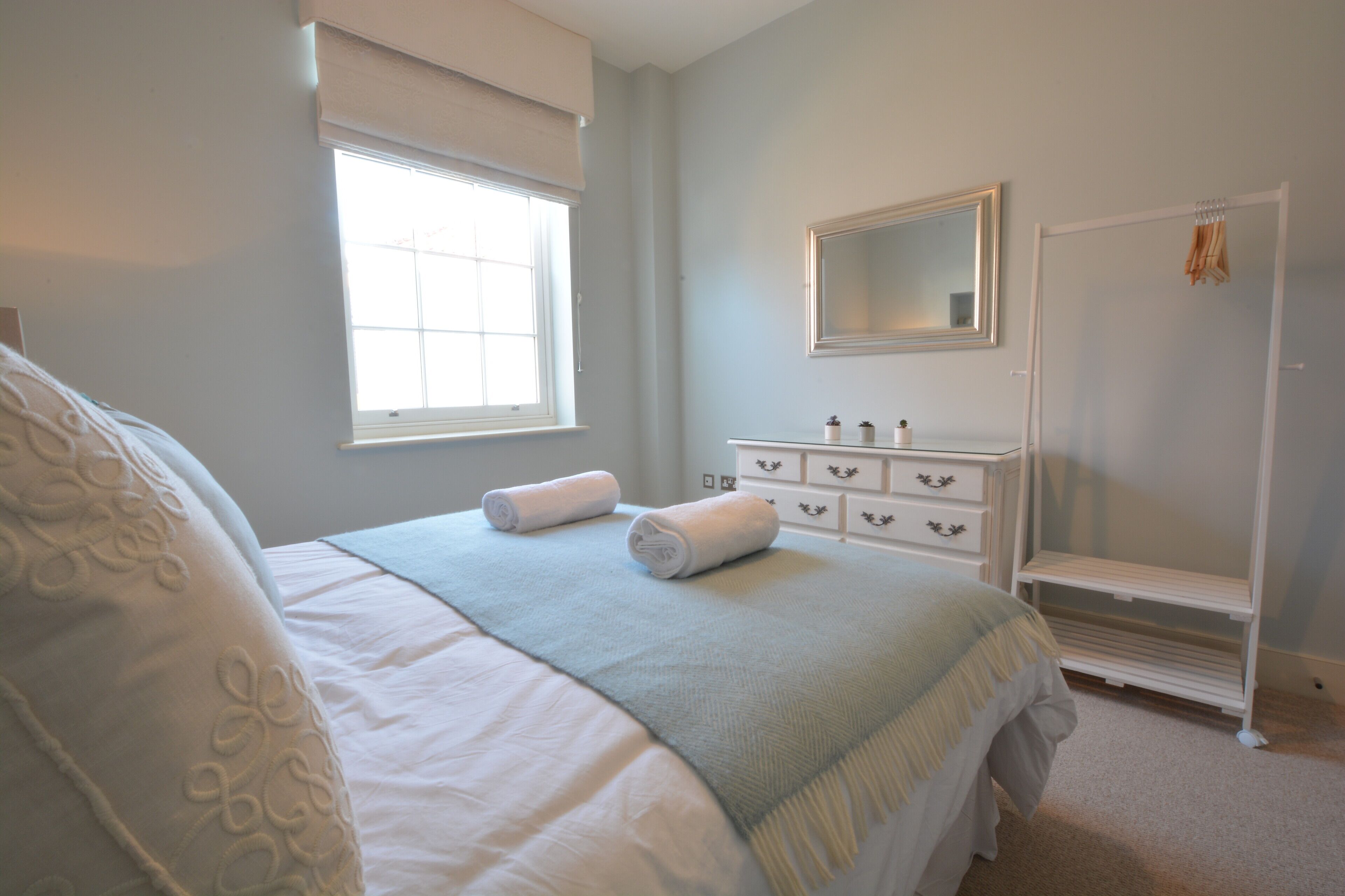 A bedroom with a bed, a dresser, a mirror, and a window.