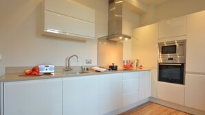 A modern kitchen with white cabinetry, a stainless steel microwave, and a built-in oven. - Skimming Stones, Aldeburgh (Aldeburgh)