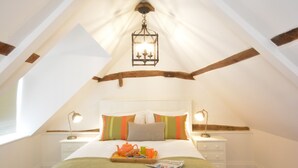 A cozy attic bedroom with a wooden beam ceiling, a hanging lantern, a bed with colorful pillows, bedside tables with lamps, and a tray with tea and snacks on the bed. - Carriage House, Bruisyard (Saxmundham)