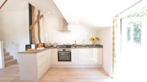 A modern kitchen with a central island, built-in oven, and a large window providing natural light. - Carriage House, Bruisyard (Saxmundham)