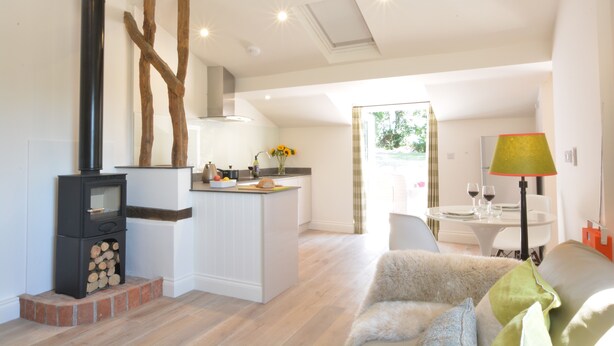 A modern living space with a central island, a fireplace, and a dining area with a table and chairs. - Carriage House, Bruisyard (Saxmundham)