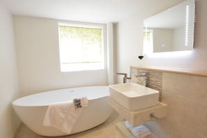 Un baño moderno con una bañera independiente, un tocador con espejo y una ventana que proporciona luz natural.