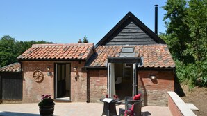 A brick building with a tiled roof, a patio with outdoor furniture, and a large potted plant. - Carriage House, Bruisyard (Saxmundham)