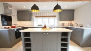 A modern kitchen with grey cabinetry, a central island, pendant lighting, and a view of the dining area. - Woodland Cottage, Great Glemham (Saxmundham)