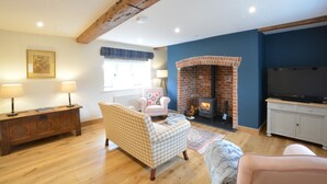 A cozy living room with a fireplace, wooden furniture, and a television. - Woodland Cottage, Great Glemham (Saxmundham)