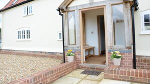 A house with a white exterior, a red-tiled roof, and a wooden front door. There are two flower pots on the steps. - Woodland Cottage, Great Glemham (Saxmundham)