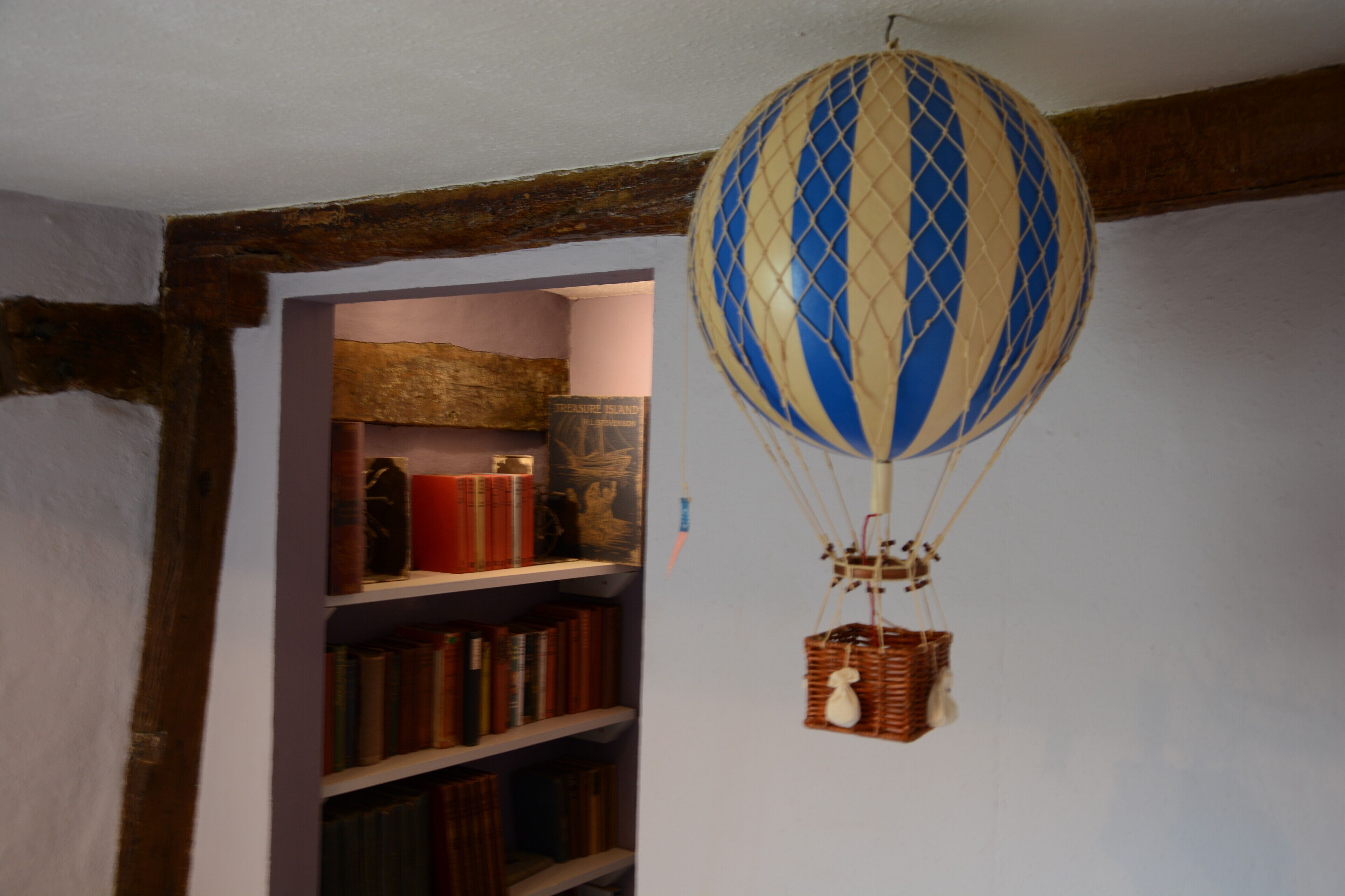 Une pièce avec une bibliothèque et une montgolfière suspendue au plafond.