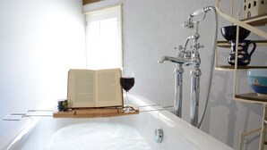 A bathtub with a book and a glass of red wine on a tray.