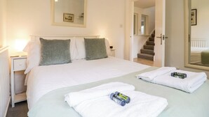A hotel room with a large bed, a nightstand, a mirror, and a view of a staircase leading to another room. - The Bridge House, Southwold (Reydon)