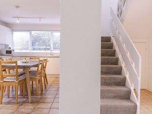 A modern kitchen with a dining area, a staircase, and a view of the outside. - The Bridge House, Southwold (Reydon)