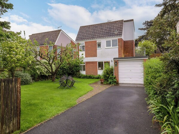 A residential building with a paved driveway, a garage, and a small garden area with a lawn and a metal table. - The Bridge House, Southwold (Reydon)