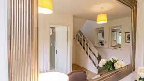 A room with a large mirror, a round table, and a chair. There is a staircase with a railing and a door leading to another room. - The Bridge House, Southwold (Reydon)