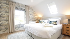 A bedroom with a large bed, a nightstand, a lamp, and a window with curtains. - The Red Brick House, Aldeburgh (Aldeburgh)