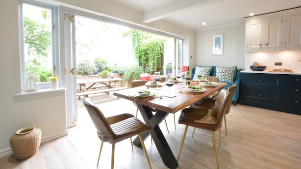 A modern kitchen with a dining table set for four, wooden flooring, and a view of the garden through large windows. - The Red Brick House, Aldeburgh (Aldeburgh)