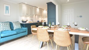 A modern kitchen with white cabinets, a dining table set for four, and a blue sofa with patterned cushions. - The Red Brick House, Aldeburgh (Aldeburgh)