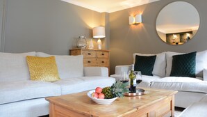 A modern living room with a white sofa, a wooden coffee table with fruits and wine, and a round mirror on the wall. - The Red Brick House, Aldeburgh (Aldeburgh)