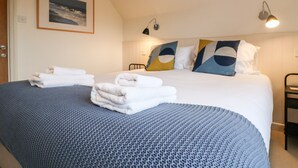 Una cama bien tendida con sábanas blancas y una manta azul, un cuadro en la pared y una lámpara de noche.