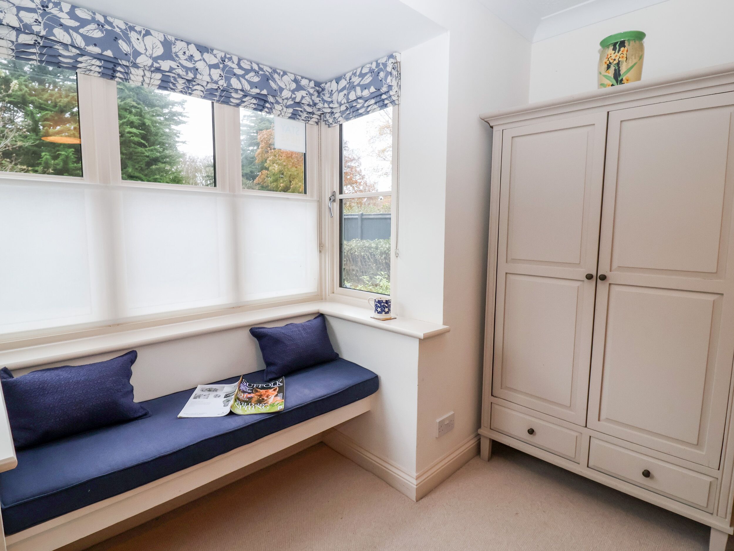 A corner room with a built-in bench, a window with a view, and a cabinet.