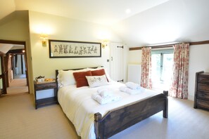 A bedroom with a large bed, a bedside table, a framed picture on the wall, and a window with curtains. - Rectory Farm Cottage, Rougham (Bury St Edmunds)