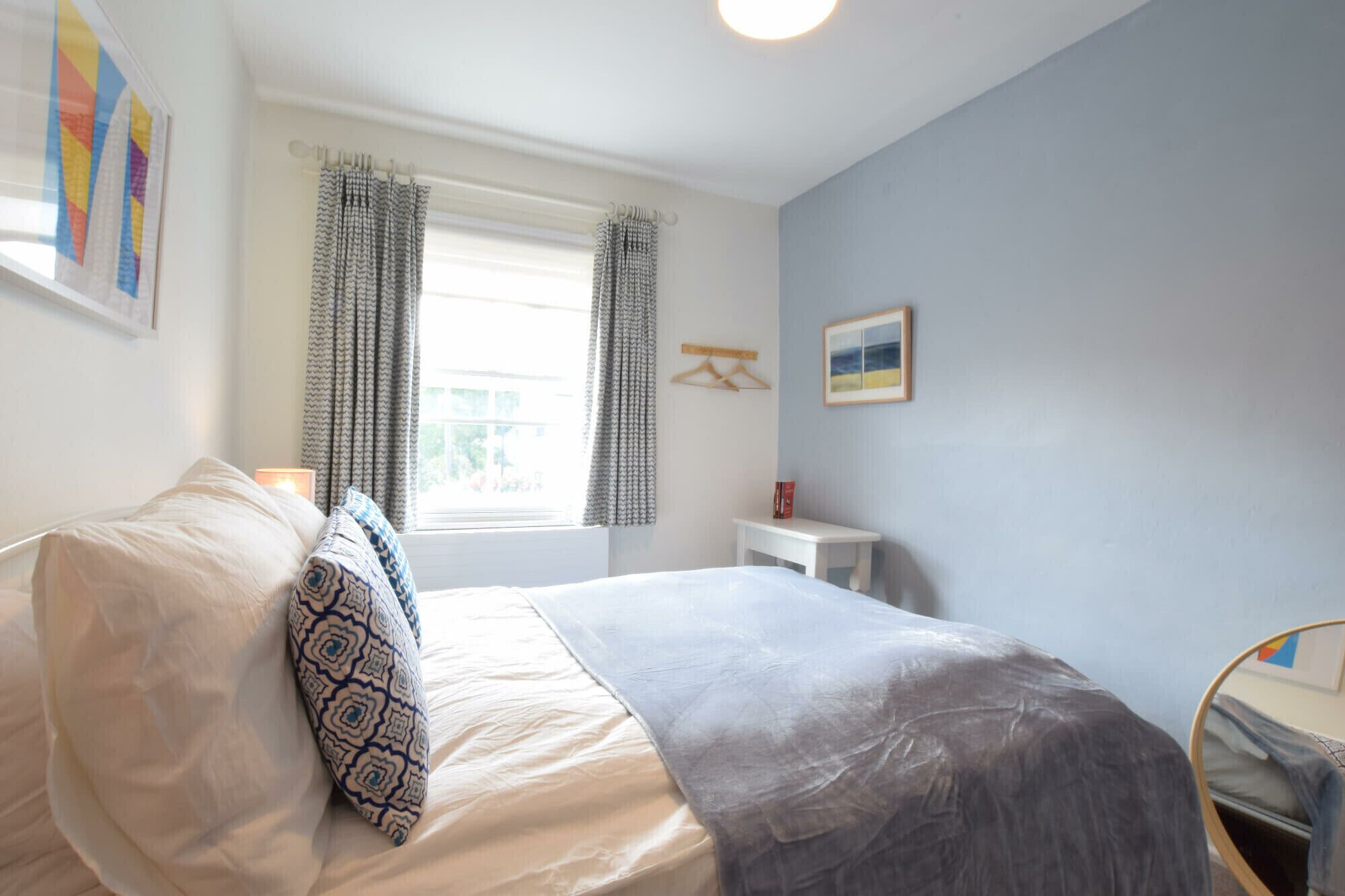 A bedroom with a bed, a bedside table, a window with curtains, and a wall-mounted picture.
