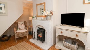 A cozy living room with a white fireplace, a television on a white cabinet, a wicker chair, and a wooden floor. - Rosemary Cottage, Aldeburgh (Aldeburgh)