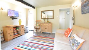 A cozy living room with a sofa, a colorful striped rug, a wooden cabinet, and a television. - Church Farm Cottage, Dunwich (Saxmundham)