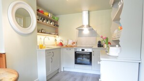 A compact kitchen with white cabinets, a built-in oven, and a stainless steel range hood. - Church Farm Cottage, Dunwich (Saxmundham)