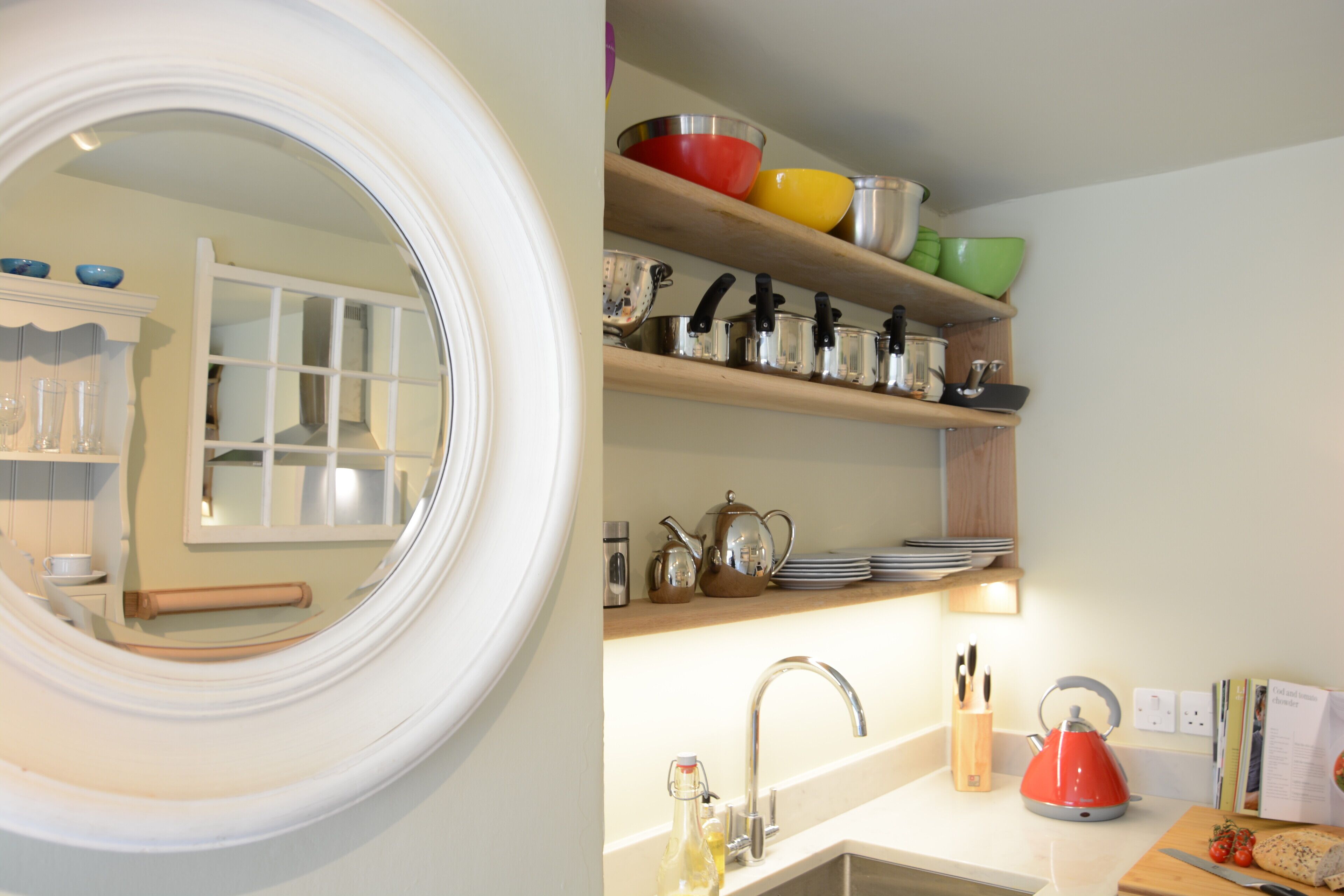 A kitchen with a round mirror, shelves with various kitchenware, a sink, and a cutting board with tomatoes.