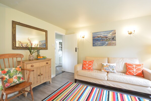 Una sala de estar con una silla de madera, un sofá color beige, un tapete con rayas de colores, un mueble de madera y un espejo en la pared.