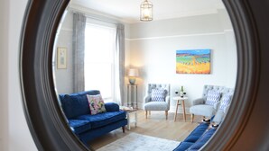 Un salon moderne avec un canapé bleu, deux fauteuils, une table basse et un tableau accroché au mur.