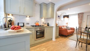 A modern kitchen with light green cabinets, a built-in oven, and a countertop with a cutting board and vegetables. - 53 Tern Cottage, Aldeburgh (Aldeburgh)