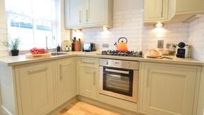 A kitchen with light green cabinets, a stainless steel oven, a gas stove, and a window with blinds. - 53 Tern Cottage, Aldeburgh (Aldeburgh)