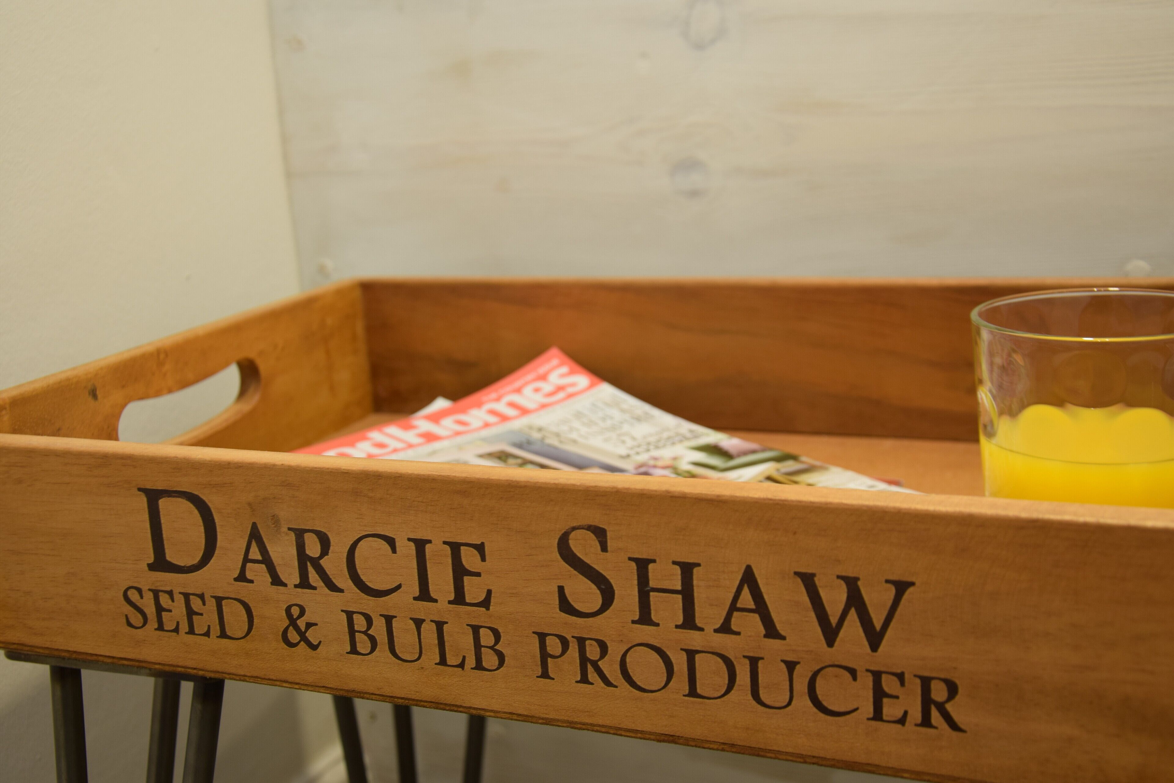 A wooden crate labeled "Darcie Shaw Seed & Bulb Producer" with a glass of orange juice.
