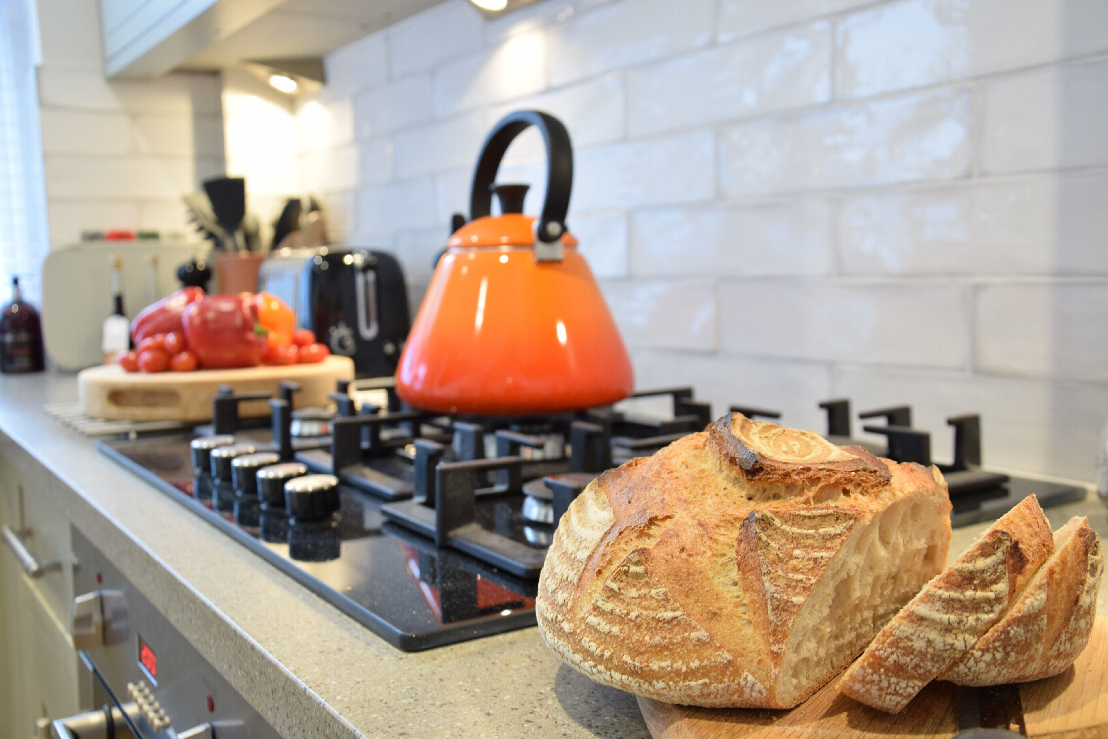 A kitchen with a gas stove, a red kettle, and a loaf of bread on the counter.
