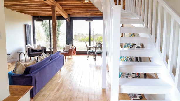Un vaste espace de vie doté d’un plafond en bois, d’un canapé bleu, d’une table à manger avec des chaises et d’un escalier blanc.