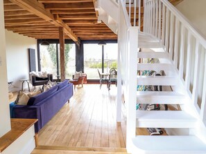A spacious living area with a wooden ceiling, a blue sofa, a dining table with chairs, and a white staircase. - Fishpond House, Sotherton (Beccles)