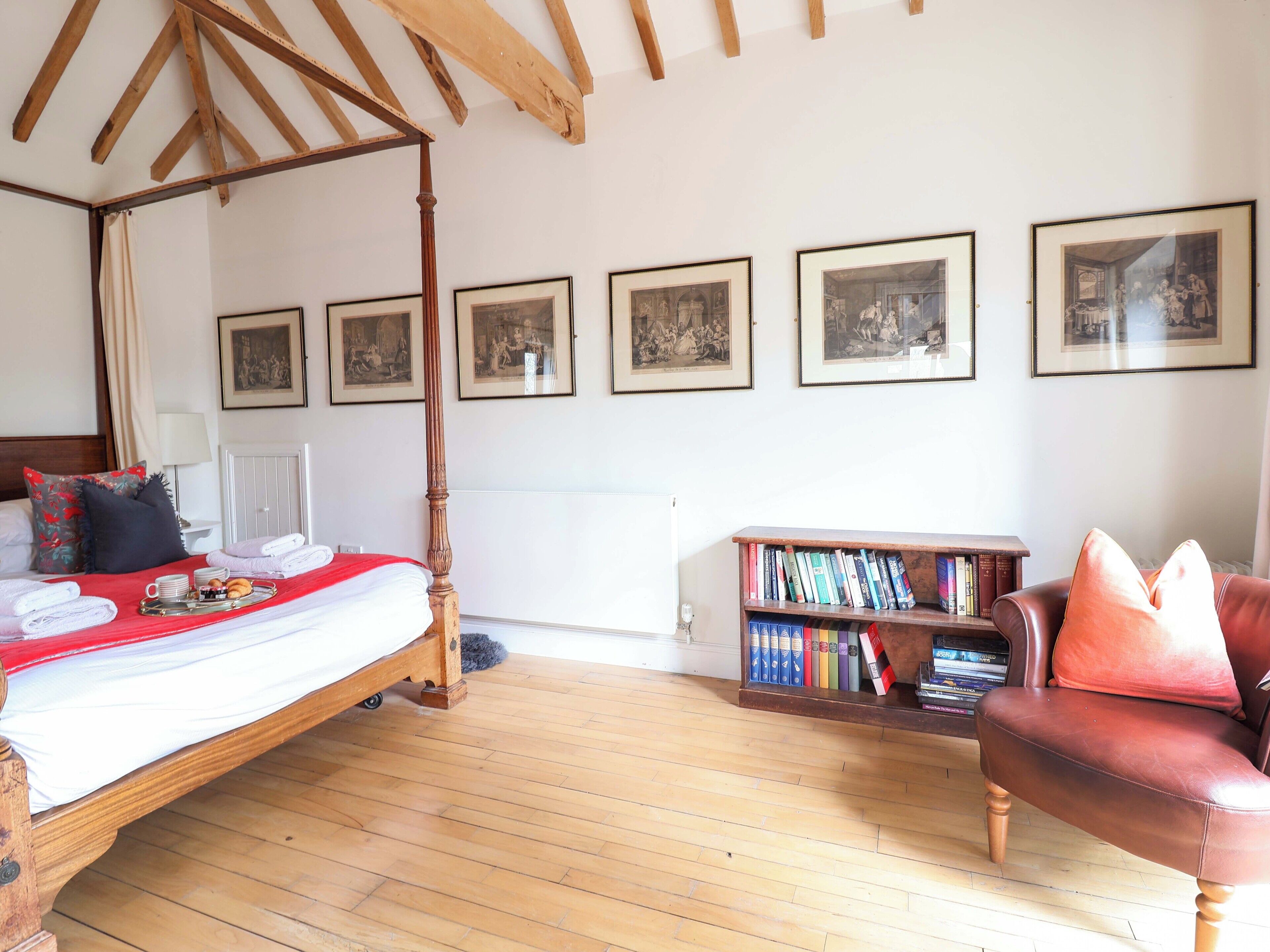 Een slaapkamer met een hemelbed, een boekenplank en ingelijste foto’s aan de muur.