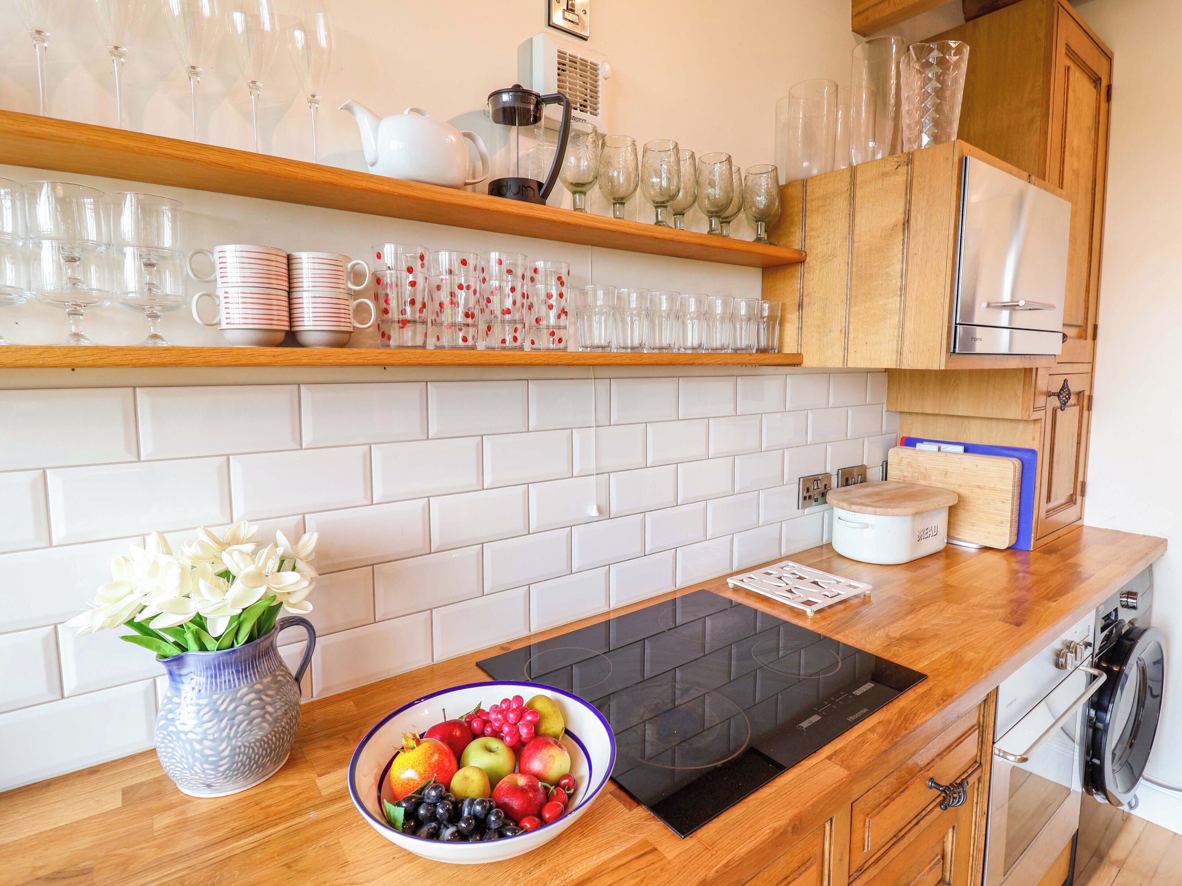 Una cocina con salpicadero de azulejos blancos, armarios de madera y una placa de inducción negra.