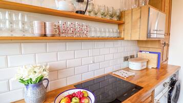 Una cocina con salpicadero de azulejos blancos, armarios de madera y una placa de inducción negra.