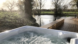 Un bain à remous avec une terrasse en bois et une vue sur une rivière paisible et des arbres.