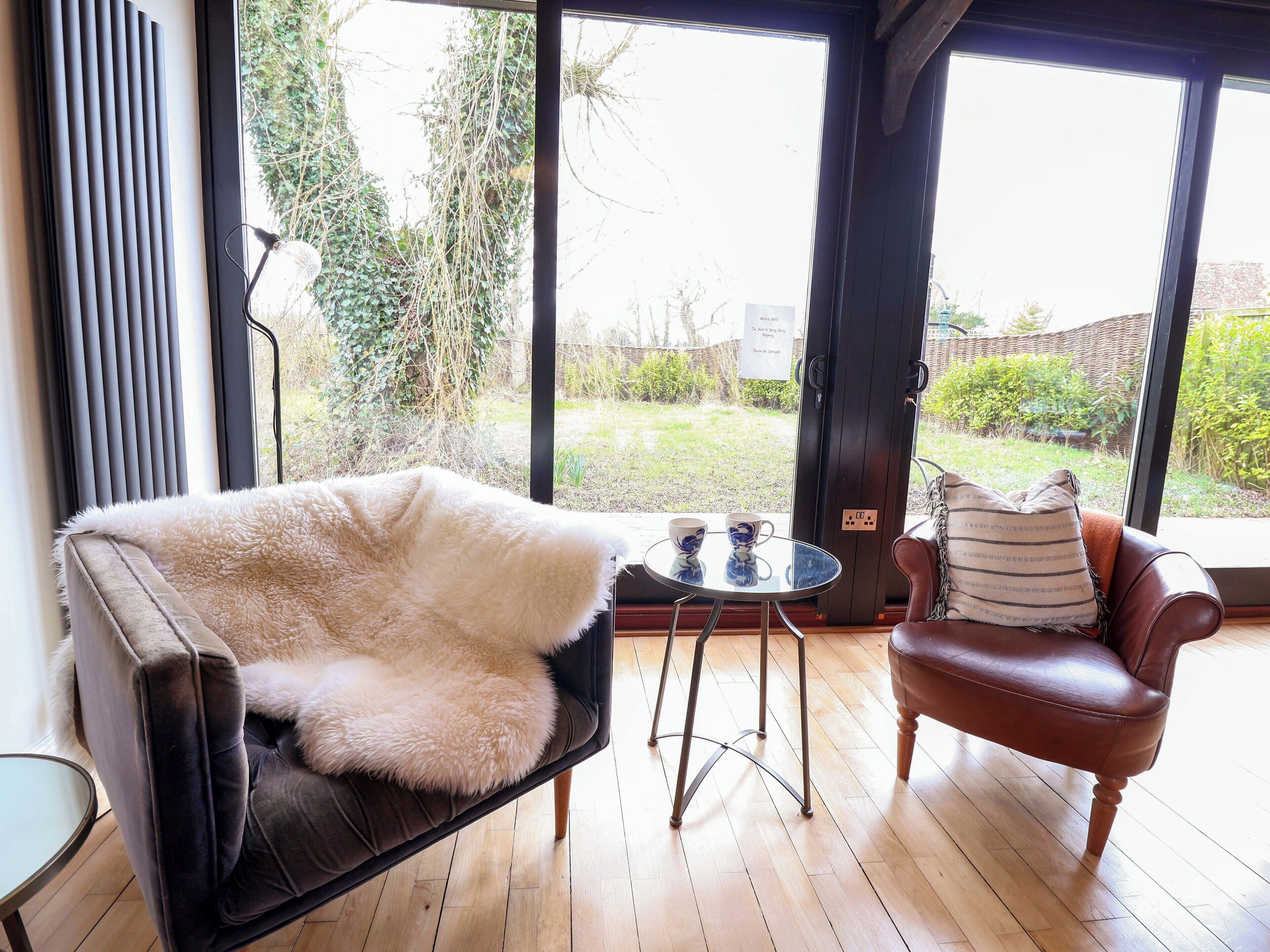 Una habitación acogedora con una butaca blanca y mullida, un sillón de cuero marrón y una mesita con dos tazas.
