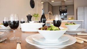 Una mesa de comedor preparada con copas de vino, una botella y ensaladas en cuencos.