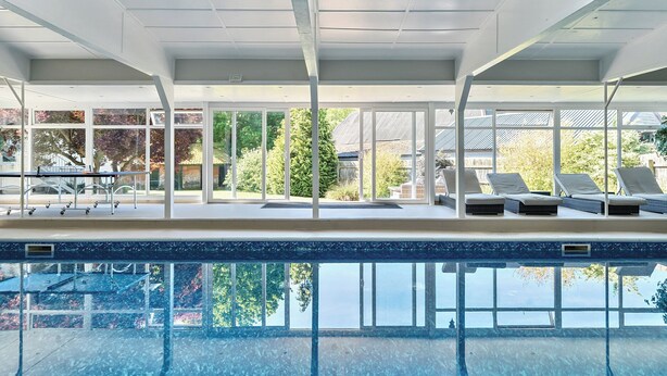 Une piscine intérieure avec des parois en verre transparent, des chaises longues et une vue sur les environs.