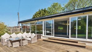 Un espace extérieur aménagé, abrité et doté de mobilier en osier et d'une structure en verre.