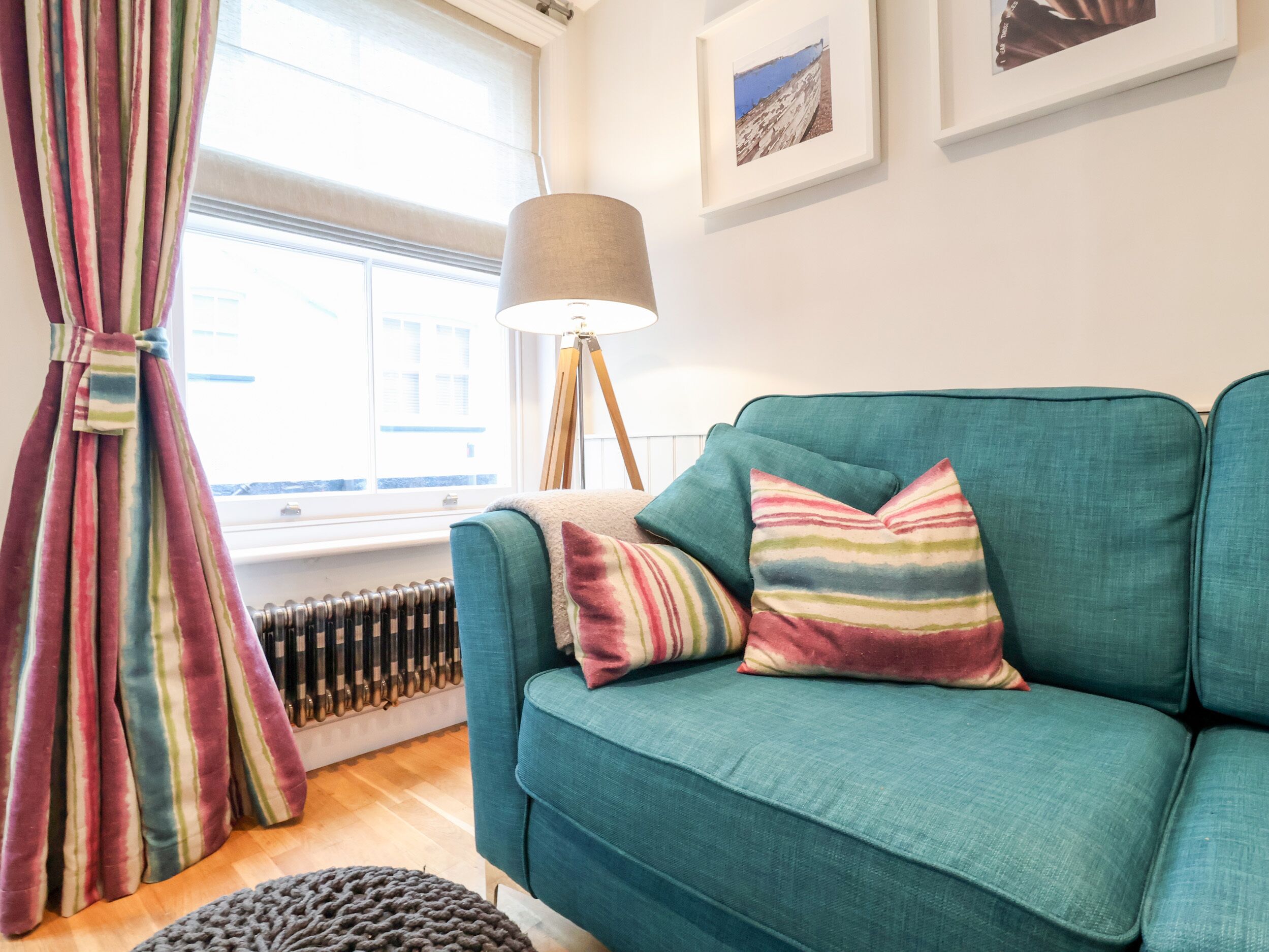A teal sofa with striped pillows, a floor lamp, and a radiator in a room with a window and curtains.