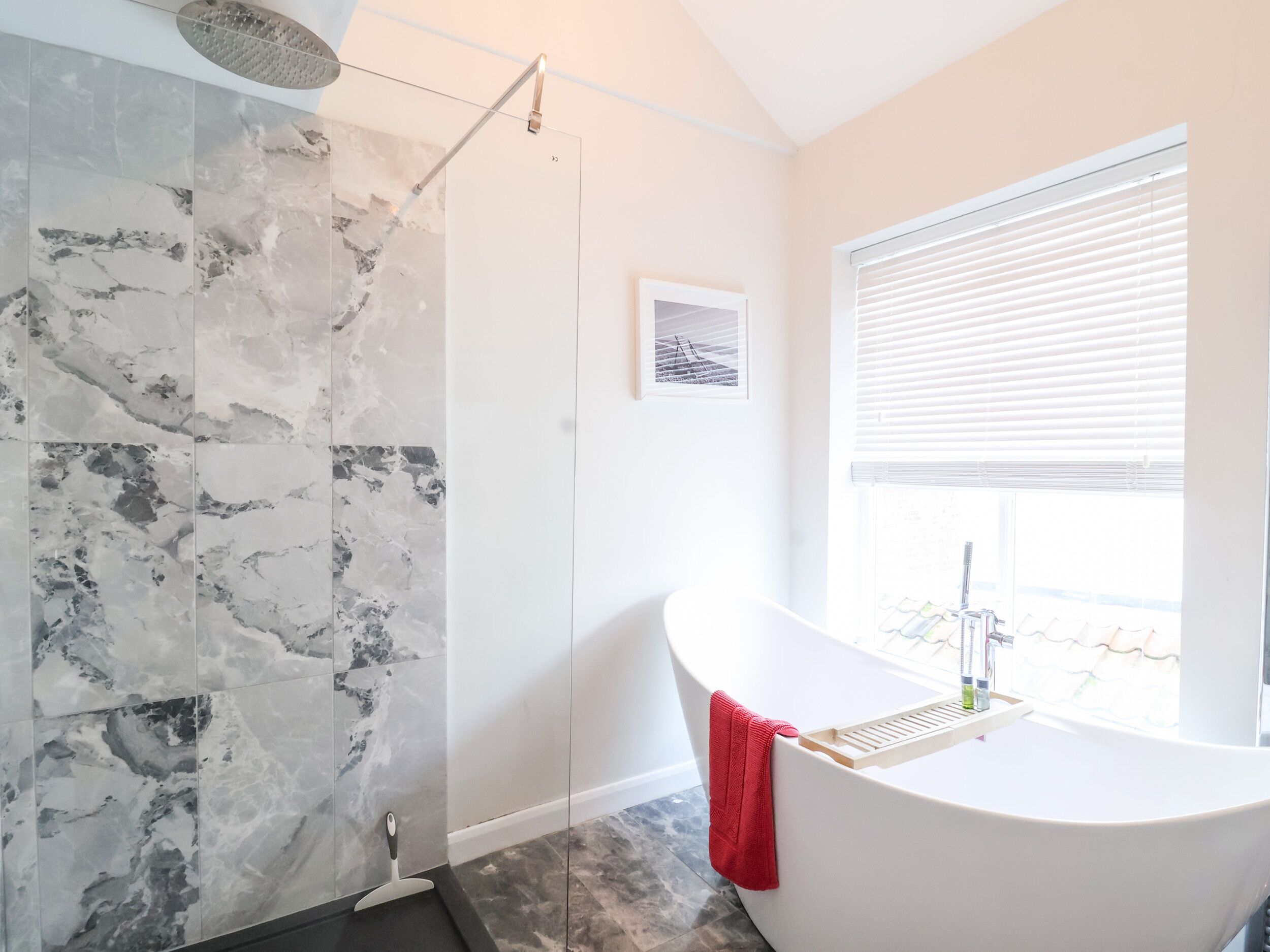 Un baño moderno con una bañera independiente, zona de ducha con puerta de cristal y ventana con persianas.