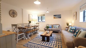 A living room with a dining area, a sofa, a coffee table, and a patterned rug. - Corner Cottage, Thorpeness (Leiston)
