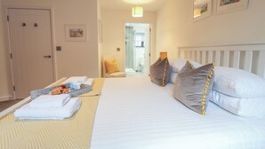 A hotel room with a bed, a chair, a tray with towels, and a door. - Corner Cottage, Thorpeness (Leiston)