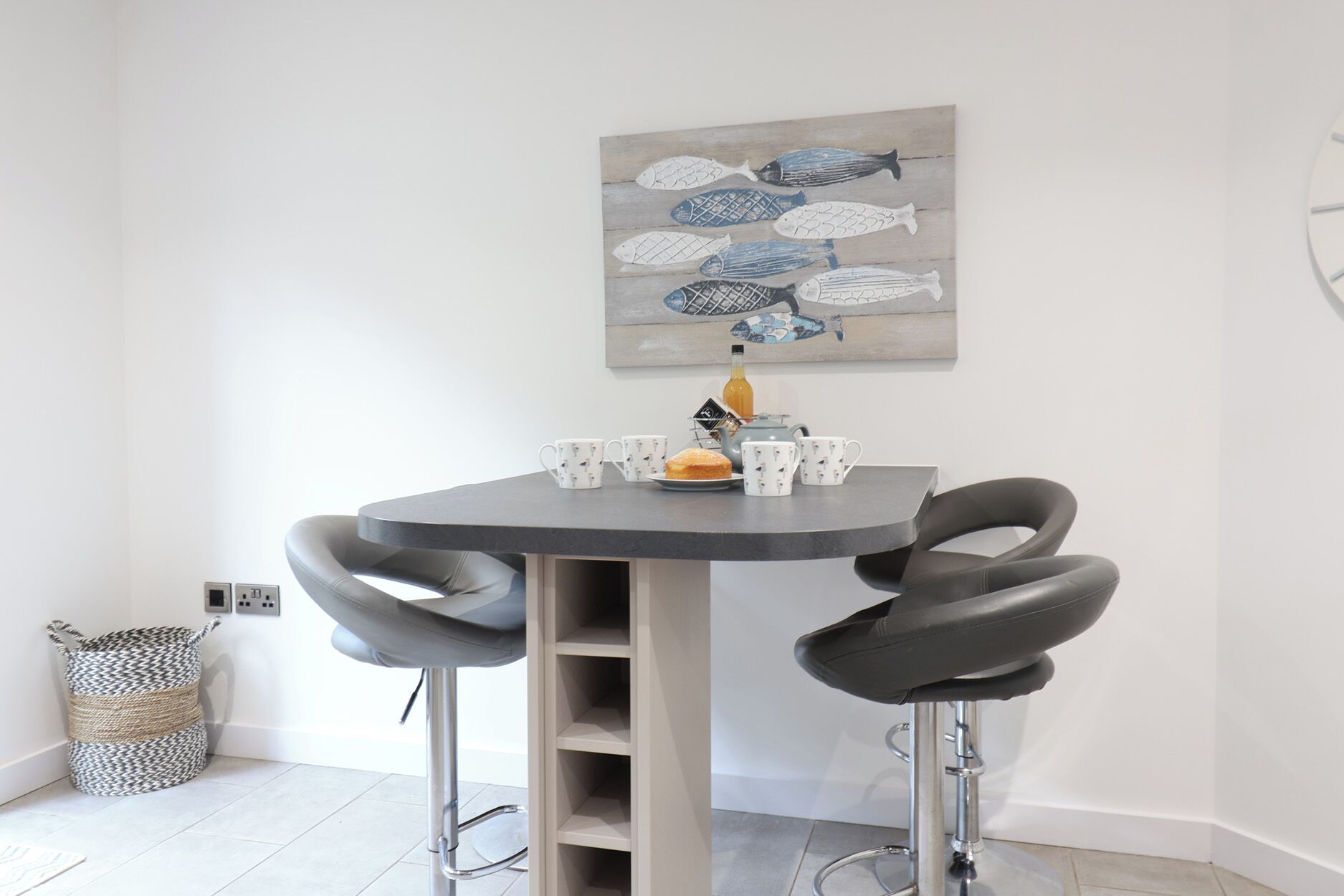 A modern dining area with a round table, two black chairs, and a decorative fish painting on the wall.