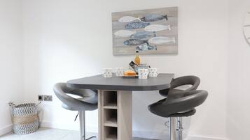 A modern dining area with a round table, two black chairs, and a decorative fish painting on the wall.